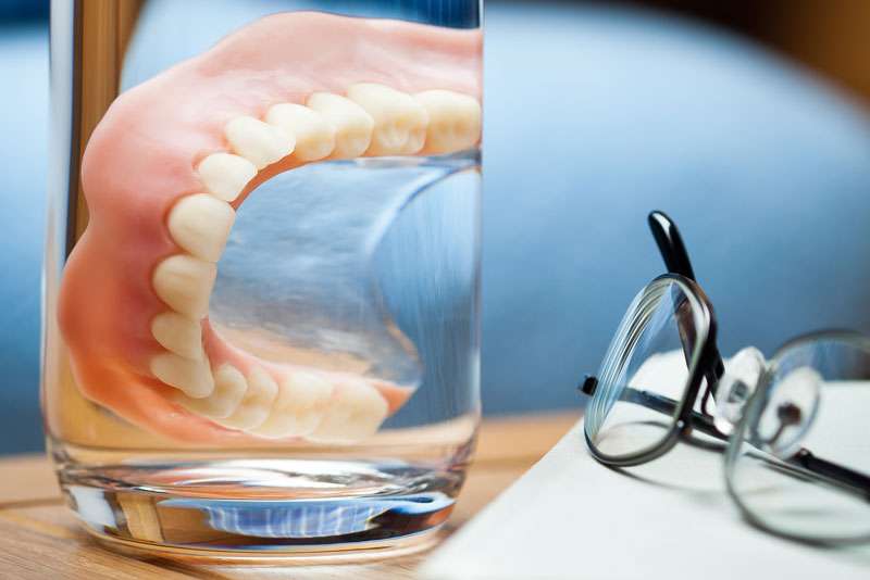 traditional dentures in a glass of solution.